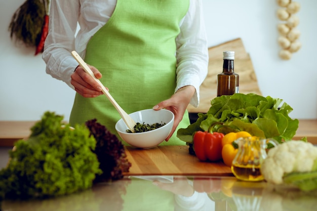 Mãos humanas desconhecidas cozinhando na cozinha. Mulher está ocupada com salada de legumes. Refeição saudável e conceito de comida vegetariana.