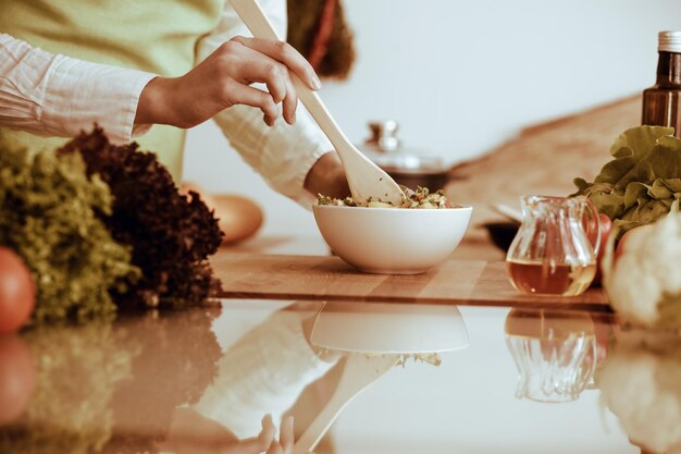 Mãos humanas desconhecidas cozinhando na cozinha. Mulher está ocupada com salada de legumes. Refeição saudável e conceito de comida vegetariana.