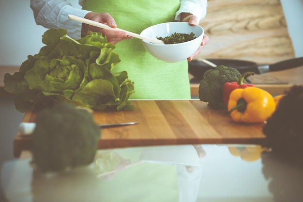 Mãos humanas desconhecidas cozinhando na cozinha. Mulher está ocupada com salada de legumes. Refeição saudável e conceito de comida vegetariana.