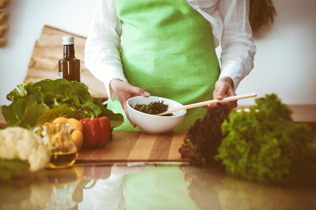 Mãos humanas desconhecidas cozinhando na cozinha. Mulher está ocupada com salada de vegetais. Refeição saudável e conceito de comida vegetariana.