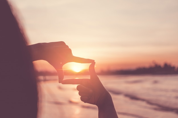 Mãos humanas, fazendo um quadro assinar sobre o céu do sol.