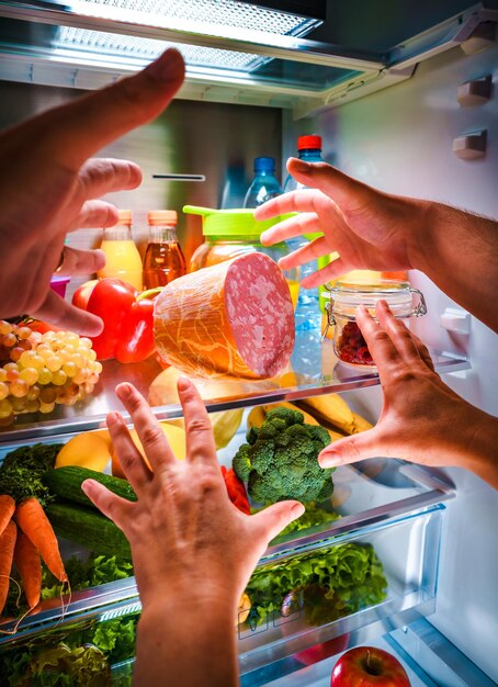 Mãos humanas pegando comida à noite na geladeira aberta