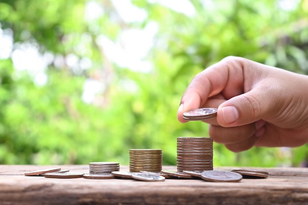 Mãos humanas segurando moedas e pilhas de moedas em ideias financeiras e de investimento de piso de madeira.