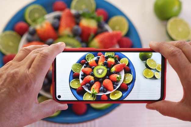 Mãos humanas tiram uma fotografia de um prato azul servido com frutas frescas da estação cruas