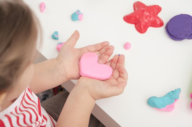 Mãos infantis com jogos de coração de plasticina rosa com massinha de modelar para modelar conjunto para presente de criatividade para o dia das mães