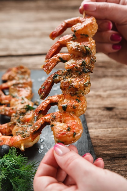 Foto mãos irreconhecíveis segurando um espeto de madeira com vista de close up de camarões fritos deliciosos. restaurante japonês de luxo.