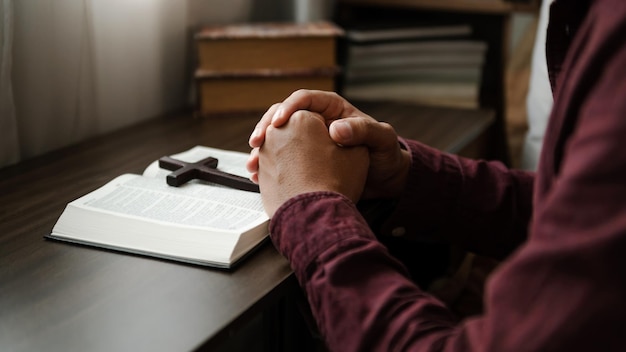 Mãos juntas em oração a Deus junto com a bíblia No conceito cristão e religião a mulher reza na Bíblia na mesa de madeiraxA