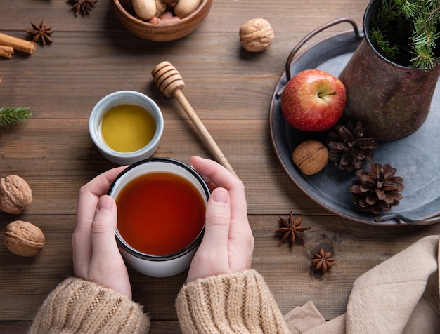 Mãos mantenham a xícara de chá de maçã aroma de natal com canela em uma mesa de madeira. vista do topo