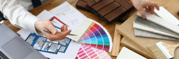 Mãos masculinas acima da mesa na qual amostras de materiais de acabamento e esquemas de cores estão localizados.