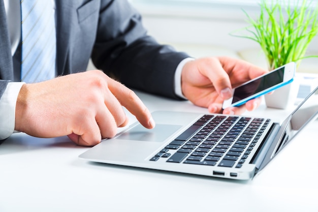 Mãos masculinas com telefone no laptop na mesa do escritório