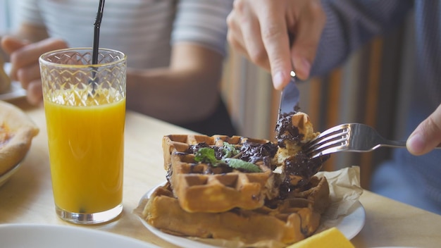 Mãos masculinas cortam waffles belgas gostosos com faca e garfo no restaurante, close-up