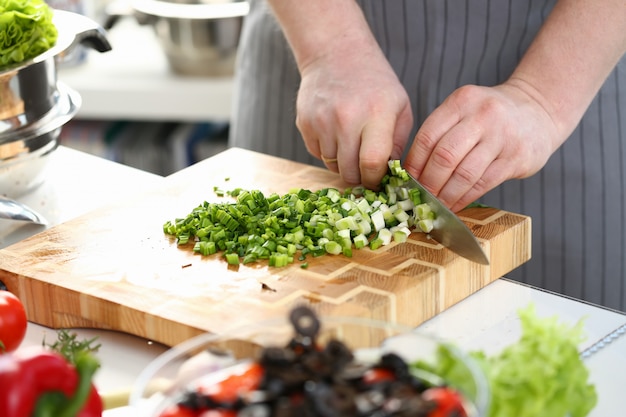 Mãos masculinas cortando ingrediente de cebolinha para salada