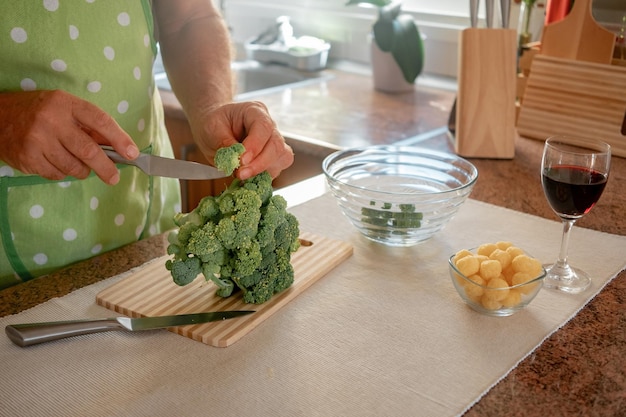 Mãos masculinas cortando repolho de brócolis saudável na tábua de madeira Conceito de alimentação saudável