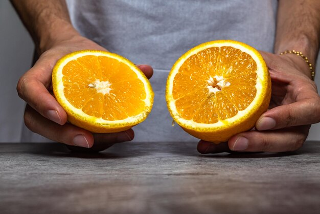 Mãos masculinas cortando uma laranja madura com uma faca em uma mesa de ardósia. Vista frontal.