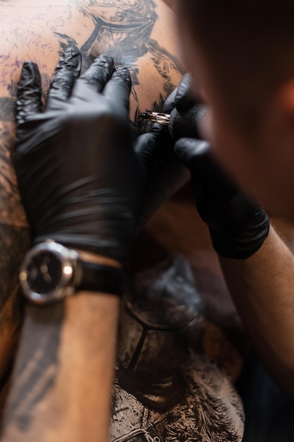 Mãos masculinas de um tatuador em luvas pretas com uma máquina de tatuagem faz uma tatuagem na pele, close-up