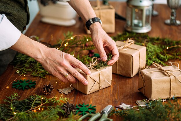 Mãos masculinas decorando a caixa de presente de artesanato de Natal com galho de abeto na mesa de madeira