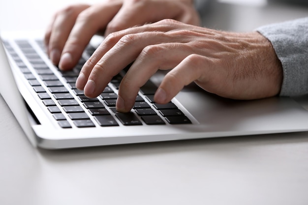 Mãos masculinas digitando no teclado do laptop na mesa fechada