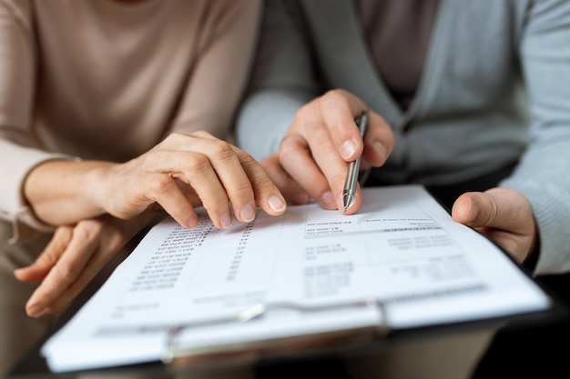 Mãos masculinas e femininas apontando para o documento enquanto discutem os termos e pontos do contrato