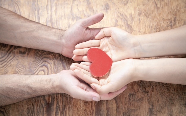 Mãos masculinas e femininas segurando um coração vermelho.