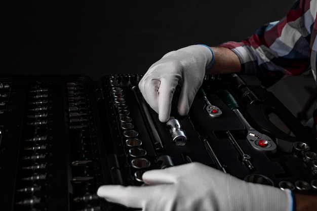 Mãos masculinas em luvas brancas de construção sobre o kit de ferramentas aberto com várias ferramentas de metal para carros e reparos domésticos, closeup.