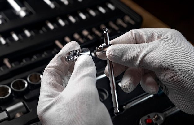 Mãos masculinas em luvas sobre a caixa de ferramentas aberta com diferentes ferramentas de metal para automóveis e reparos domésticos, close-up.