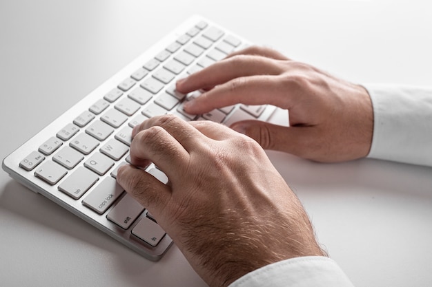 Mãos masculinas em um teclado branco sobre um fundo branco. Conceito de negócios.