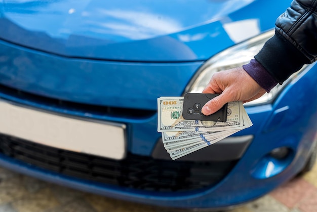 Mãos masculinas em um terno de negócios seguram dólares e chaves de carro em um fundo de carros azuis