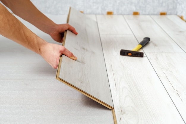 Mãos masculinas está colocando o painel de madeira de piso laminado dentro de casa close-up. Piso laminado, cópia espaço