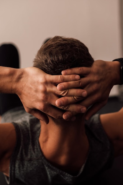 Mãos masculinas fortes atrás da cabeça de um atleta que realiza um exercício esportivo