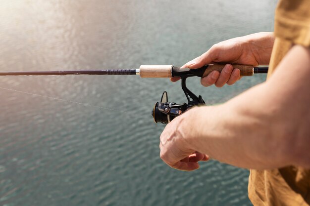 Mãos masculinas hoolding vara giratória, colher-isca e pesca na água azul, close-up.