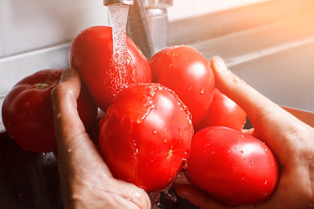 Mãos masculinas lavam tomates. Tomates grandes sob fluxo de água. Parte do café da manhã natural. As vitaminas são sempre importantes.