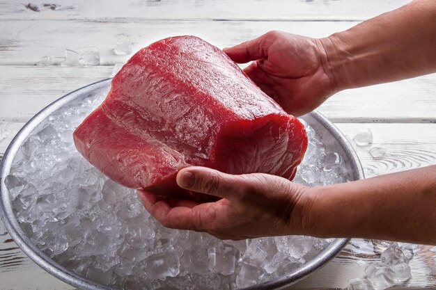 Mãos masculinas seguram um prato de carne de peixe com gelo e um pedaço enorme de carne de atum não estraga a comida