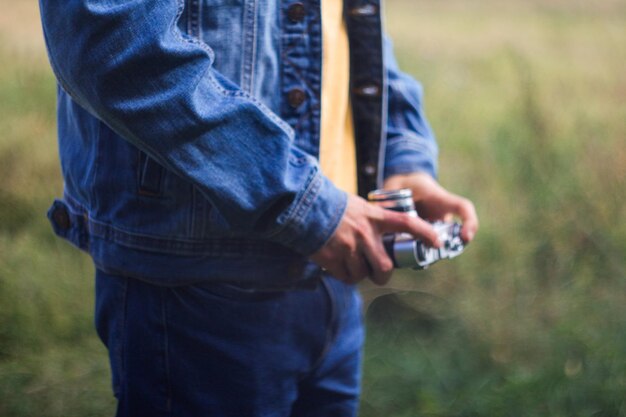 Mãos masculinas segurando câmera retrô em fundo de natureza verde filme efeito de grão homem de calça jeans