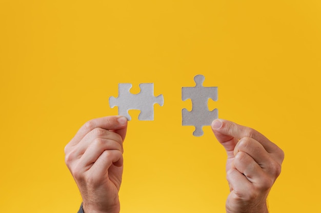 Mãos masculinas segurando duas peças do puzzle correspondentes em branco sobre fundo amarelo.