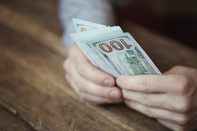 Mãos masculinas segurando notas de dólar na velha mesa de madeira