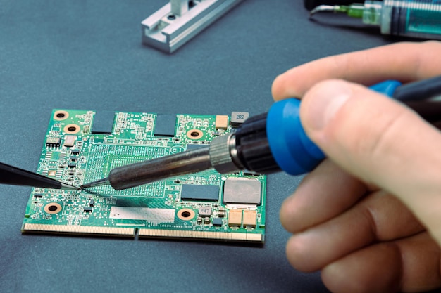 Mãos masculinas segurando um ferro de solda para soldar o resistor na placa do computador. conserto de equipamento de informática