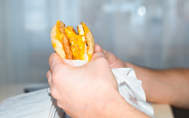 Mãos masculinas segurando um grande hambúrguer com costeleta, queijo e ovos fritos, close-up dentro de casa.