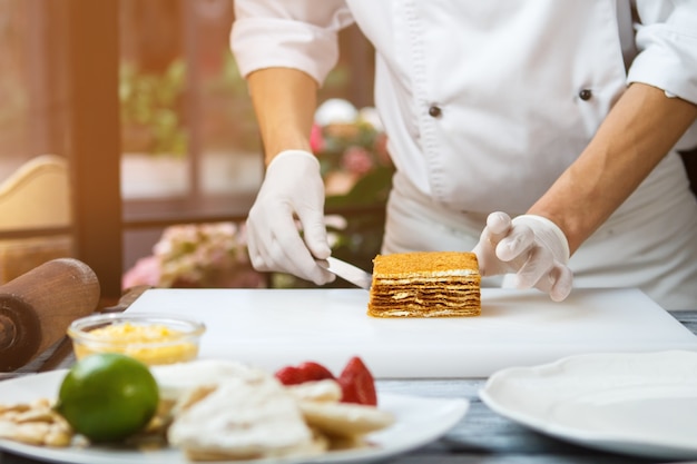 Mãos masculinas tocando o bolo. Bolo na placa de cozinha branca. Bolo de mel preparado pelo chef. Sobremesa doce na cozinha do restaurante.