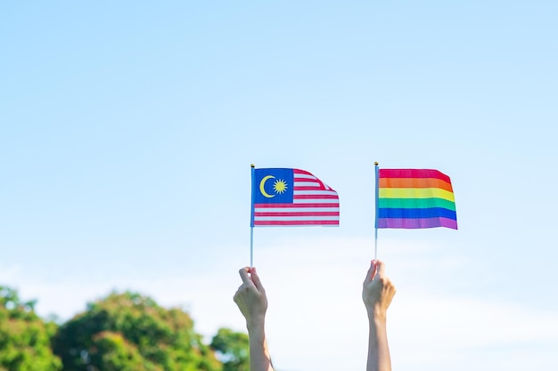 Foto mãos mostrando a bandeira lgbtq rainbow e malásia no fundo da natureza apoie a comunidade lésbica gay bissexual transgênero e queer e o conceito do mês do orgulho