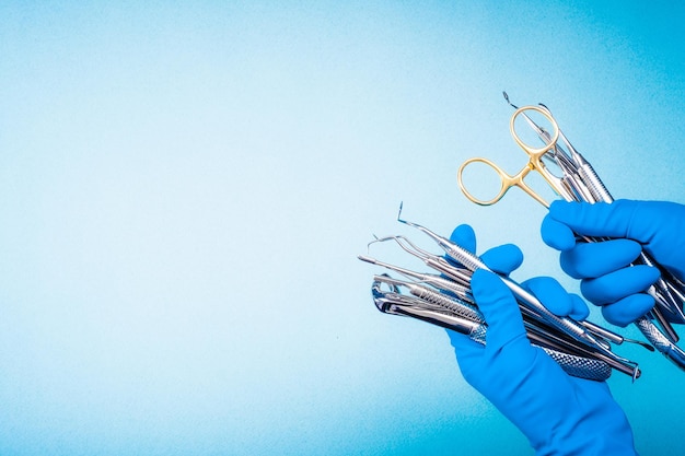 Mãos nas luvas azuis segurando um equipamento odontológico de cirurgia em fundo azul claro