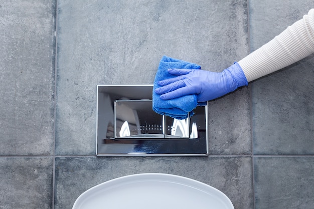 Foto mãos nas luvas de proteção para limpar o botão de descarga do banheiro
