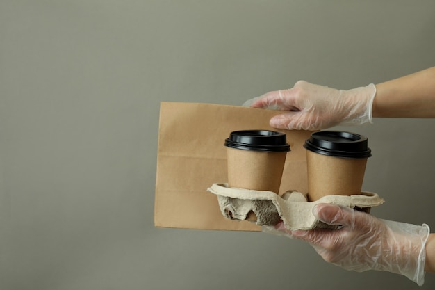 Mãos nas luvas seguram copos de papel e bolsa cinza
