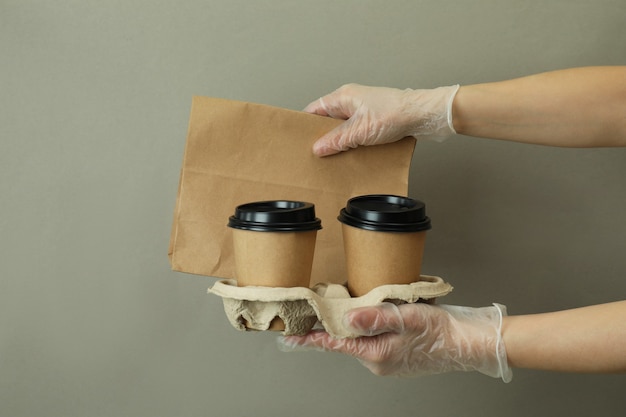 Mãos nas luvas segurando copos de papel e bolsa em fundo cinza