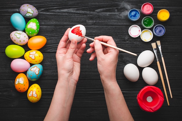 Mãos pintando ovos para o feriado da Páscoa na mesa de madeira