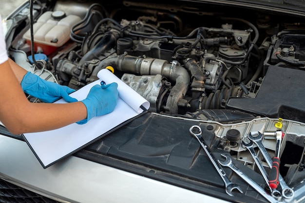 Mãos próximas de uma jovem mecânica sorridente realizando diagnósticos em um carro