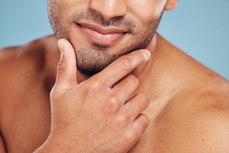 Foto mãos rosto e beleza com um modelo de homem posando no estúdio em um fundo azul para cuidados com a pele ou higiene limpeza de banheiro e bem-estar com um jovem homem dentro de casa para promover um produto cosmético natural