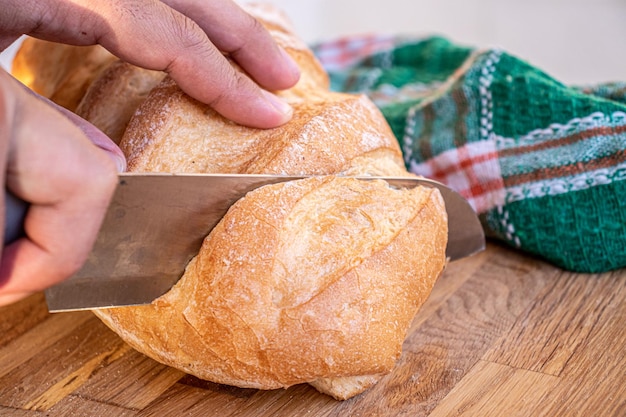 Mãos segurando a faca e cortando o pão em fatias a serem servidas