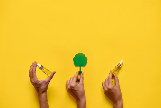 Foto mãos segurando árvores e óleos essenciais. medicina natural plana leigos. amarelo