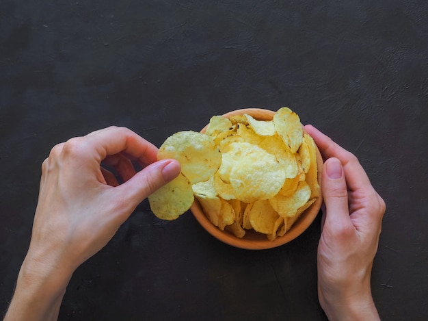 Mãos segurando batatas fritas numa superfície escura