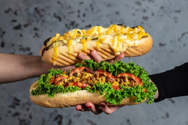 Mãos segurando cachorros-quentes totalmente carregados com coberturas variadas. cachorro-quente de fast food, refeição americana de calorias pouco saudáveis. banner, menu, local de receita para texto